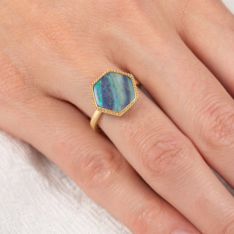 Gold ring with a hexagonal boulder opal stone on a person's finger