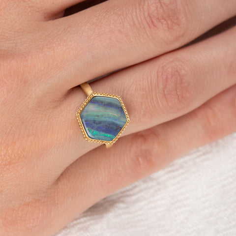 Gold ring with a hexagonal boulder opal stone on a person's finger