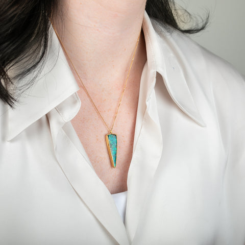 Triangle-shaped boulder opal stone pendant with a gold setting on a person