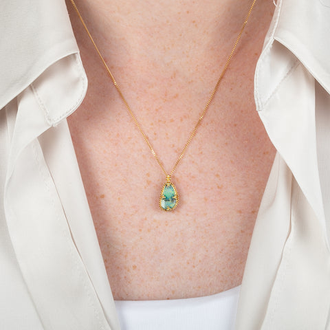 A gold necklace featuring a boulder opal gemstone worn on a person