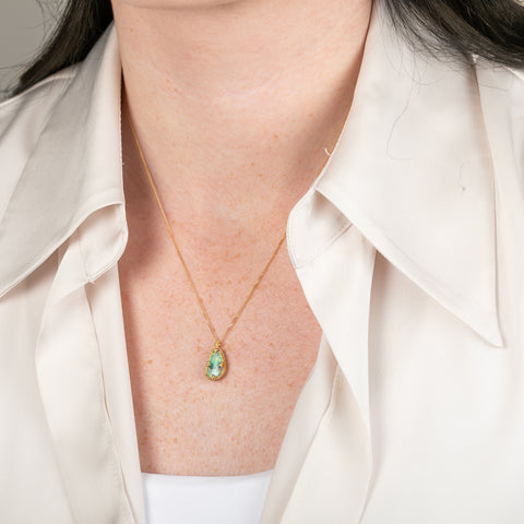 A gold necklace featuring a boulder opal gemstone worn on a person