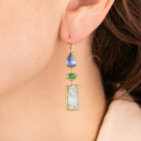 Close-up of a person wearing a gold earring with colorful gemstones.