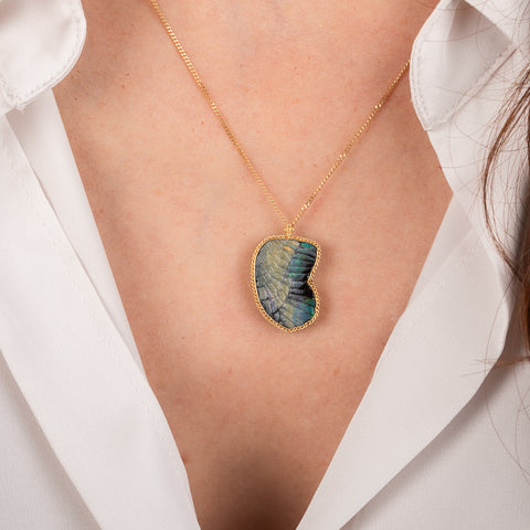 Gold necklace featuring a boulder opal carved into a wing on a person's neck