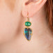 Gold earrings featuring boulder opals and emeralds worn in a person's ear