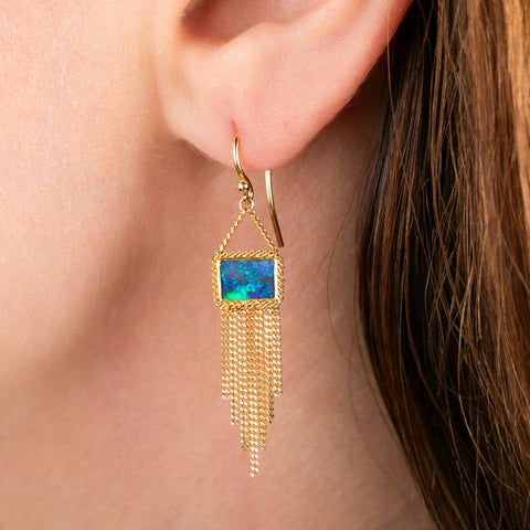 A gold drop earring featuring a rectangular boulder opal stone and cascading gold fringe, shown against a plain white background.