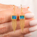 A pair of gold drop earrings featuring rectangular boulder opal stones and cascading gold fringe, shown held in hand.