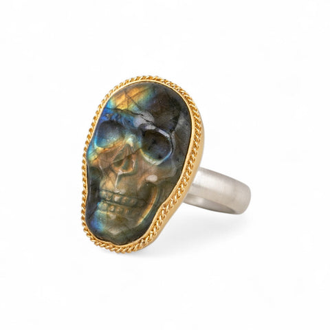 Carved labradorite skull ring with gold bezel and silver band on white background