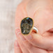 A hand holds a labradorite skull ring set in an 18k gold bezel with a sterling silver band