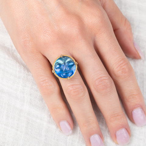 Hand wearing a gold ring with a carved moon face moonstone on a white background