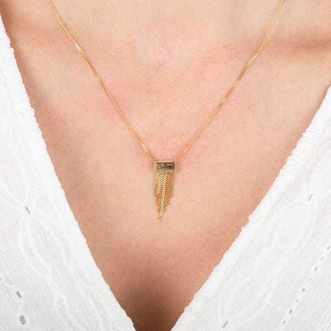 Gold necklace with a rectangular diamond and gold fringe on a person