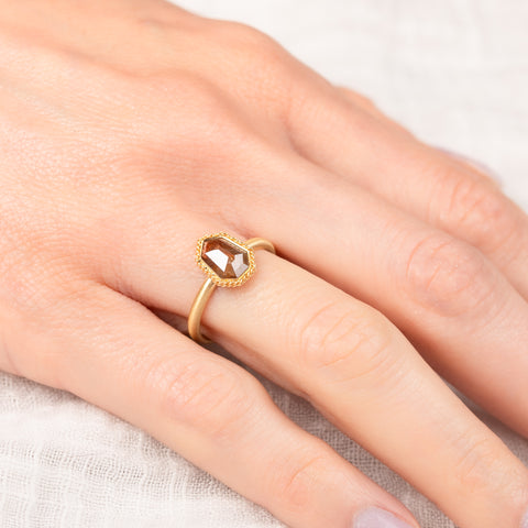 Gold ring with a diamond on a person's finger against a neutral background