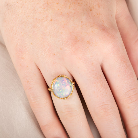 Opal ring on a person's finger with a neutral background