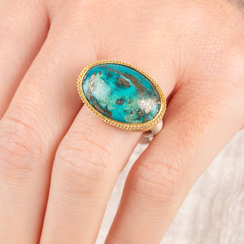 A close up of a person wearing a handmade fine jewelry turquoise ring with an 18k gold bezel and sterling silver band