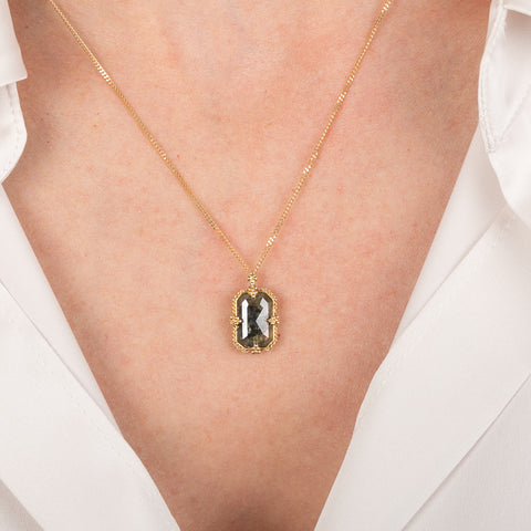 Gold necklace with a dark-colored diamond on a person wearing a white shirt