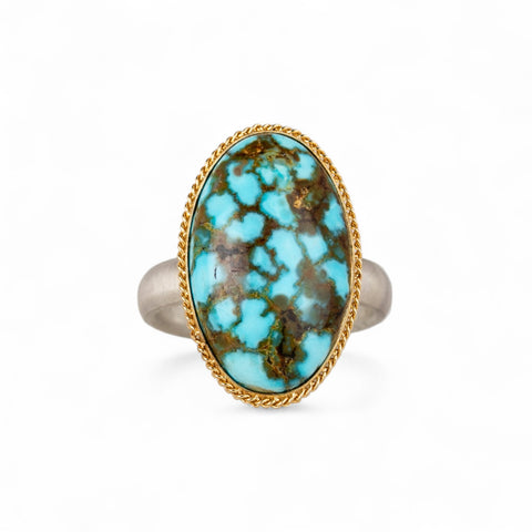 Turquoise ring with gold bezel and sterling silver band on white background