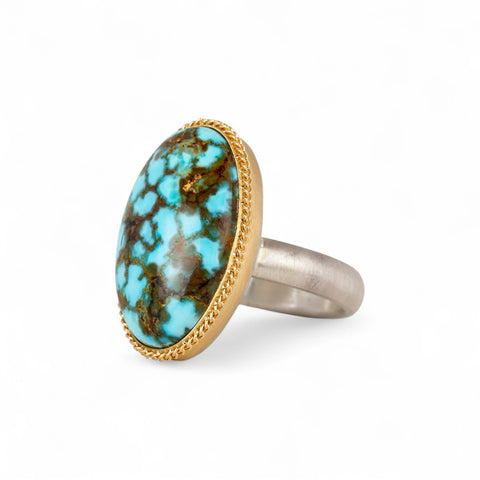 Turquoise ring with gold bezel and sterling silver band on white background