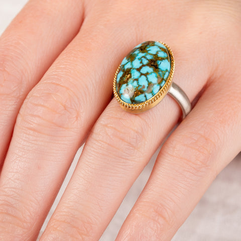 Close up of hand wearing a turquoise ring with gold bezel and sterling silver band 