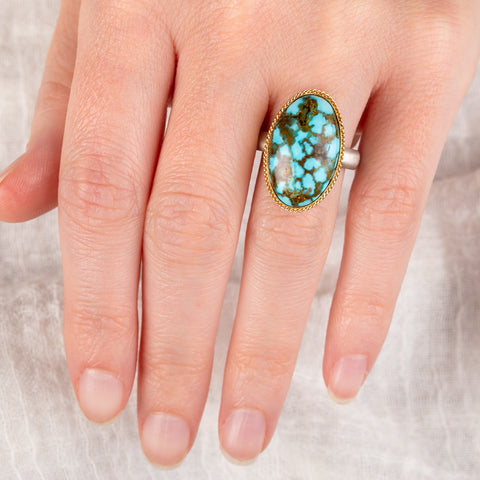 hand wearing a turquoise ring with gold bezel and sterling silver band 