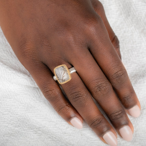A gold and silver ring featuring a dendritic quartz stone with a detailed tree branch pattern inside, on a person's finger.