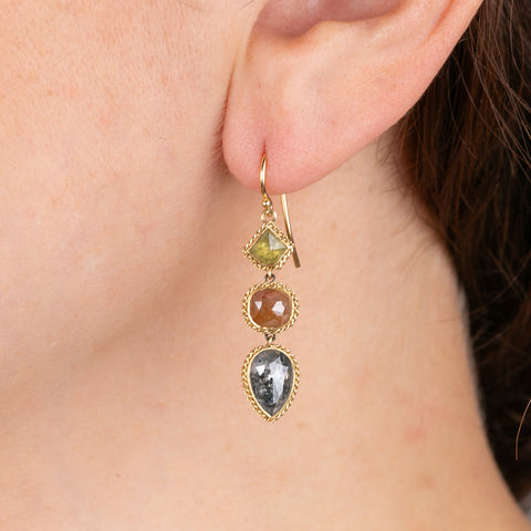 Gold earrings with three different colored diamonds worn on a person