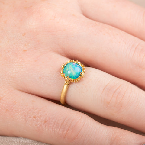 Gold ring with an Ethiopian opal stone on a person's finger