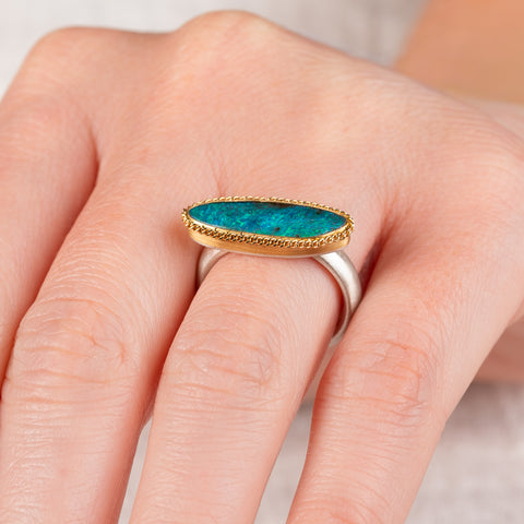 A hand wearing a boulder opal ring with an 18k gold bezel and sterling silver band