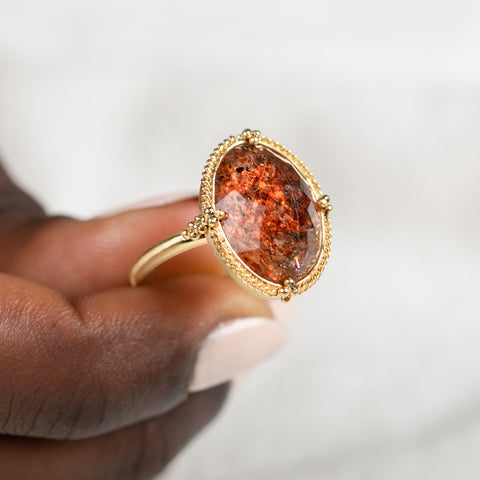 Gold ring featuring a sunstone gemstone held in hand