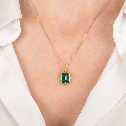 Gold necklace featuring an emerald gemstone on a person