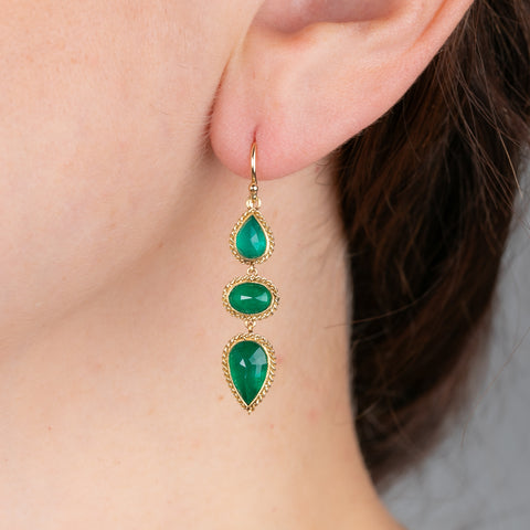 Gold earrings with emerald gemstones worn by a person