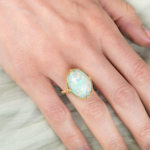 Hand wearing a gold ring with an opal stone on a light fabric background
