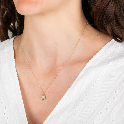 Gold necklace with an ethiopian opal teardrop pendant worn by a person in a white top.