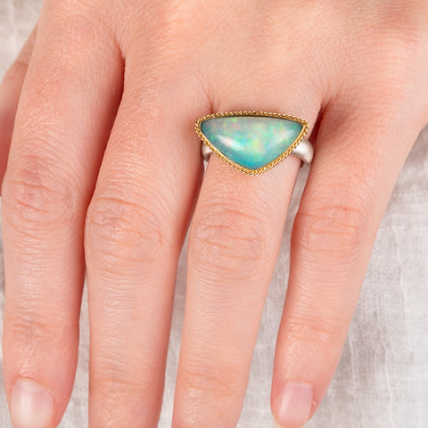 Hand wearing an Ethiopian opal ring with gold bezel and sterling silver band