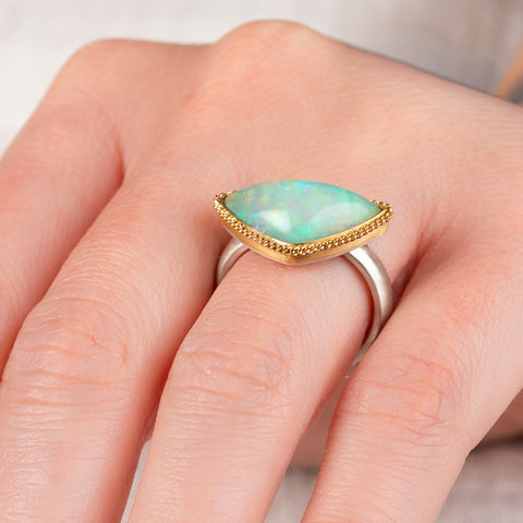 Close up of a hand wearing an Ethiopian opal ring with gold bezel and sterling silver band