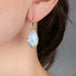 Opal teardrop earring on a person's ear with a neutral background