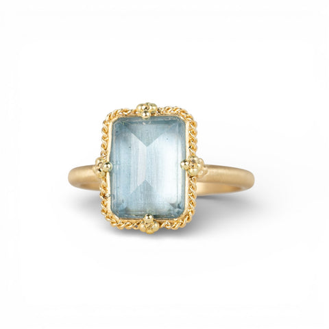 Gold ring with a rectangular aquamarine gemstone on a white background