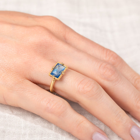 Gold ring with a blue moonstone on a hand against a light background