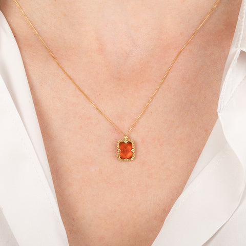 Gold necklace with a fire opal pendant on a person wearing a white shirt.