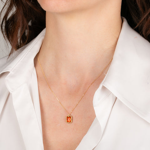 Gold necklace with a fire opal pendant worn by a person in a white shirt.