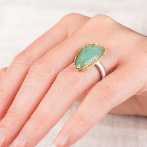 Hand wearing a ring featuring an emerald gemstone set in an 18k gold bezel with a silver band 