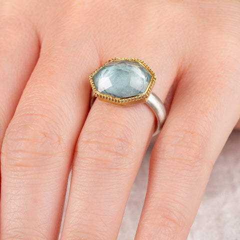 Close up of a hand wearing an aquamarine ring with 18k gold bezel and sterling silver band on white background