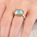 Close up of a hand wearing an aquamarine ring with 18k gold bezel and sterling silver band on white background