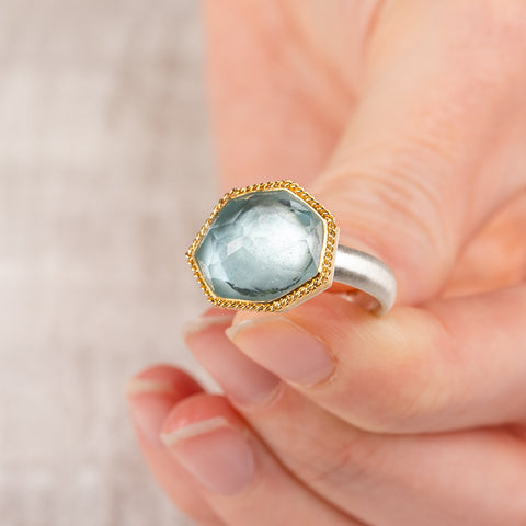 Close up of a hand holding an aquamarine ring with 18k gold bezel and sterling silver band on white background