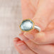Close up of a hand holding an aquamarine ring with 18k gold bezel and sterling silver band on white background