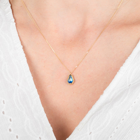 Gold necklace with a moonstone  pendant on a person wearing a white top.