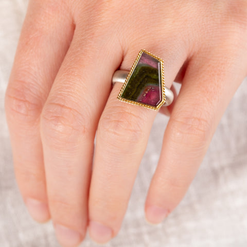 Close up of hand wearing a tourmaline ring with gold bezel and silver band