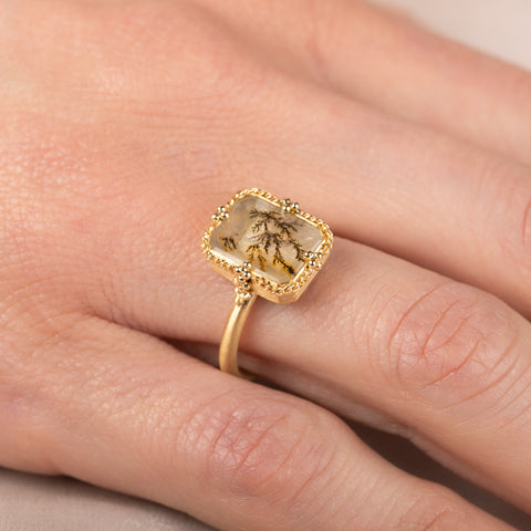 Gold ring with a dendritic quartz stone on a person's finger