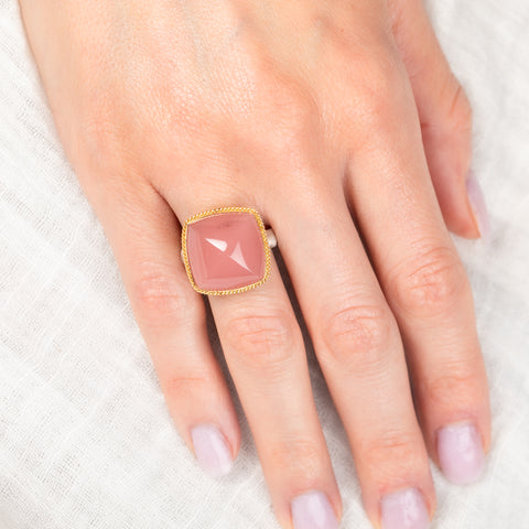 Hand wearing a ring with a pink guava quartz stone on a white background