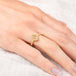 Gold ring with a golden colored diamond on a person's finger against a light background