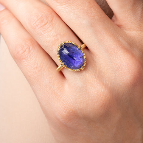 Gold ring with a tanzanite gemstone on a hand against a beige background