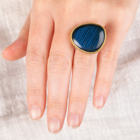 A hand wearing a ring with labradorite stone set in a gold  bezel with a silver band